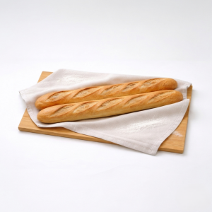 Two crusty baguettes on a wooden board partially covered by a white towel.