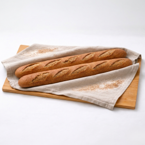 Two golden-brown baguettes on a wooden cutting board, resting on a beige linen cloth with a light flour dusting.