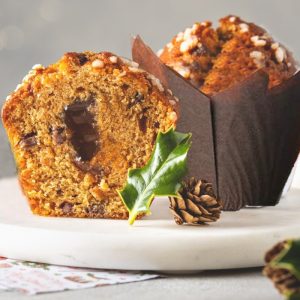 Sliced chocolate-filled spice cake on a white plate with sugared crust, holiday greenery, and a pinecone nearby