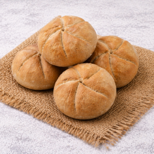 Four round rustic bread rolls with scored tops on a burlap mat.