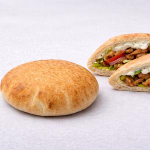 Round, golden-brown sandwich bun with a cut-open sandwich showing meat, lettuce, tomato, and creamy sauce inside a soft white roll.