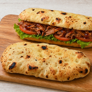 Pulled pork sandwich with lettuce and tomato on toasted flatbread, on a wooden board