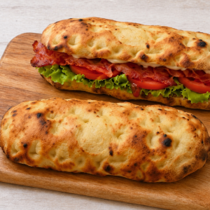 Two grilled panini sandwiches on a wooden board, filled with lettuce, tomato, bacon, and melted cheese.