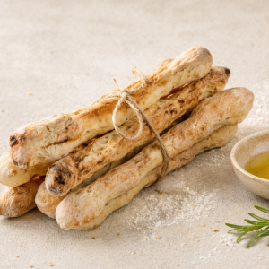 Bundle of crusty baguette bread sticks tied with twine on a flour-dusted surface, with a small bowl of olive oil nearby and a rosemary sprig nearby.